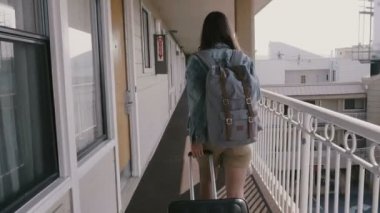 Seyahat çantası ve sırt çantasıyla Amerikan yol kenarındaki otel koridorunda yürüyen mutlu genç bir turist kadın..