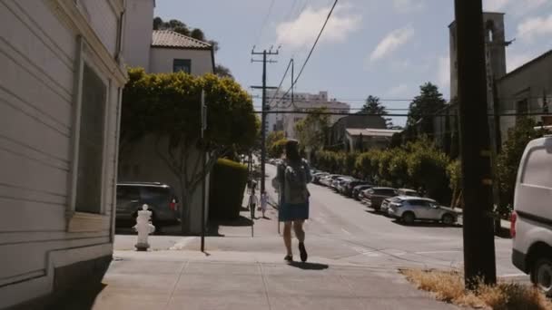 Yavaş çekim kamerası, San Francisco 'da yaz aylarında dik yolda yürüyen sırt çantalı mutlu genç turist kadını takip ediyor.. — Stok video