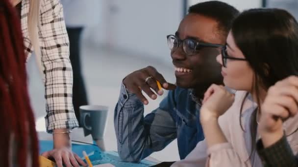 Jóvenes felices sonriendo socios de negocios multiétnicos hablando, discutiendo ideas de trabajo sobre lluvia de ideas detrás de la mesa de la oficina . — Vídeo de stock