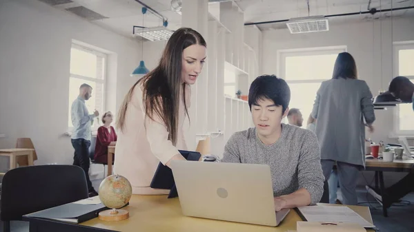 Hermosa mujer ejecutiva ayuda a colega asiático en su mesa. Gente de negocios multiétnicos trabajan en la oficina moderna 4K . — Foto de Stock