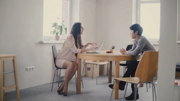 Asijský mladík mluví s jistotu podnikatelka v tabulce. Mnohonárodnostní lidé mluví v trendy moderní kanceláři 4k. — Stock fotografie