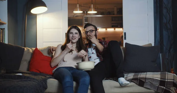 Счастливая молодая европейская романтическая пара смотрит сериал дома, улыбается и разговаривает, ест попкорн замедленной съемки — стоковое фото