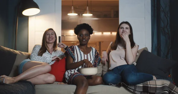 Gelukkig jong multi-etnische vrouwen vrienden zitten samen thuis kijken films lachen samen met snacks slow motion. — Stockfoto