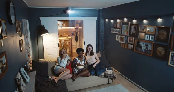 Hermosa feliz multiétnica mujeres amigos ríen viendo comedia programa de televisión en casa en pantalla grande con proyector de cámara lenta — Foto de Stock