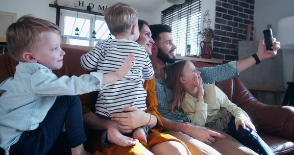 Szczęśliwa młoda, kaukaska rodzina z trójką dzieci rozmawia, macha do przyjaciół przez telefon wideo w domu w zwolnionym tempie. — Zdjęcie stockowe