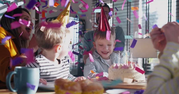 Bonito menino caucasiano criança soprando no bolo de aniversário na festa da família, o pai é surpreendido pela explosão confetti câmera lenta . — Fotografia de Stock