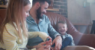 Mutlu, genç, gülümseyen, beyaz bir baba evde küçük bir kız ve oğluyla oynuyor..