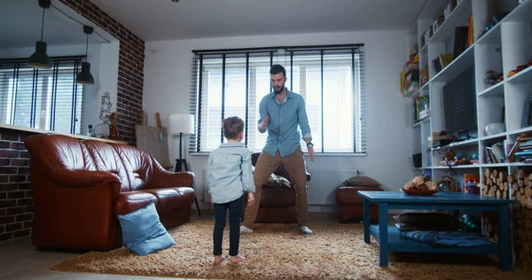 Feliz joven caucásico padre y pequeño hijo jugando, abrazando y bailando en la casa de luz moderna sala de estar cámara lenta . — Foto de Stock