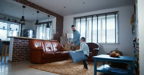 Feliz joven caucásico padre y pequeño hijo jugando, almohadas de lucha en la casa de luz moderna sala de estar cámara lenta . — Foto de Stock