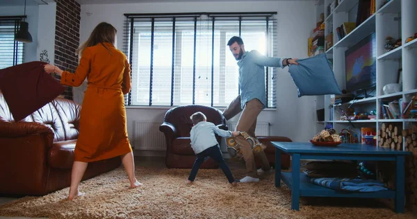 Rodinná zábava. Šťastný mladý evropský otec a matka bojovat polštáře s roztomilé malý syn v moderním domácím zpomalení — Stock fotografie