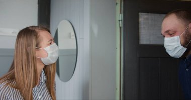 Tıbbi maske takan mutlu beyaz kadın tecrit süresince teslimatçı adamdan paket kutusu alıyor..
