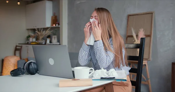 Sick young beautiful Caucasian woman coughs and sneezes with tissues, using laptop to work from home on quarantine. — Stock Photo, Image