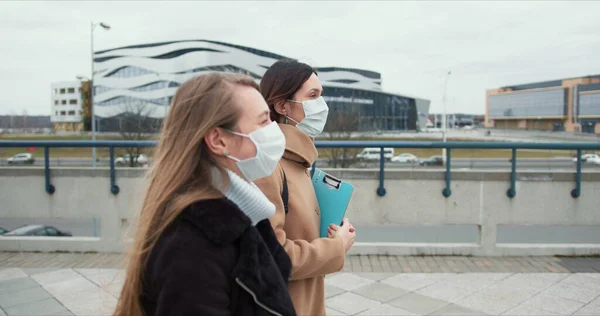 Vista lateral duas mulheres caucasianas assistentes de saúde social usam máscaras médicas andando na rua da cidade vazia em confinamento . — Fotografia de Stock