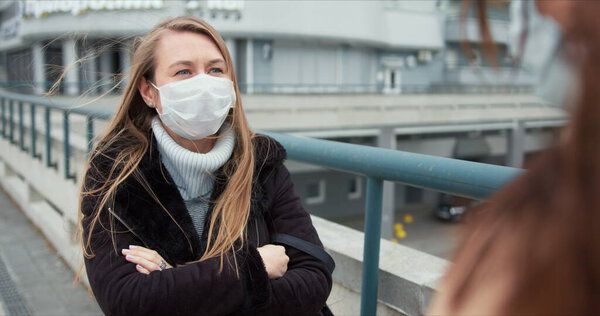 Coronavirus epidemic control. Young Caucasian female social care doctor gives consulting advice outside in medical mask.