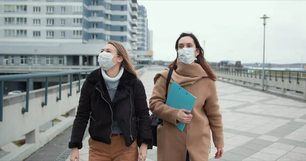 Duas jovens médicas usam máscaras andando na rua vazia e ventosa da cidade. Ambiente de medo e perigo em quarentena epidémica . — Fotografia de Stock