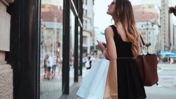 Joven mujer hermosa usando el teléfono inteligente cerca del escaparate y que girando, alejándose. Movimiento lento . — Vídeo de stock