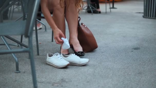 Vue rapprochée de la jeune femme assise dans la rue et changeant les chaussures avec des talons sur des baskets ou des baskets . — Video