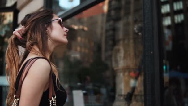 Shopping of young beautiful woman. Brunette female standing near the shop-window and looking on it. Slow motion. — Stock Video