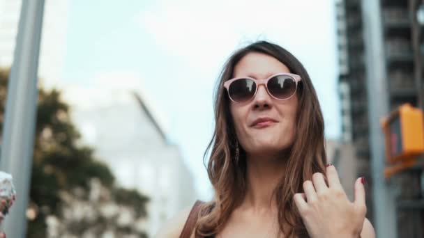 Portrait of young happy woman in sunglasses walking in downtown and eating, holding the melting ice cream with topping. — Stock Video