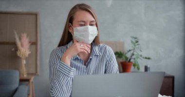 Genç, profesyonel doktor kadın, yüz maskesi takarak evdeki insanlara yardım etmek ve danışmak için bilgisayarını kullanıyor.