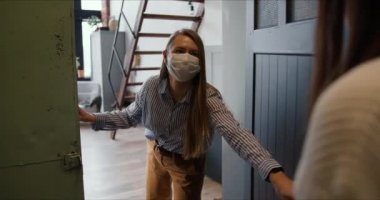 Maskeli genç beyaz kadın kuryeden tecrit çantalarını almak için apartmanın kapısını açıyor..