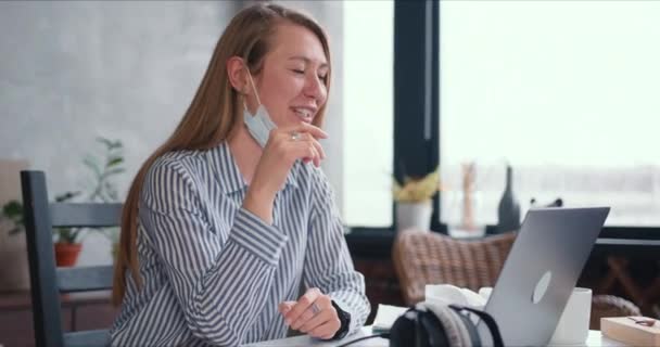 Ung frisk glad läkare kvinna gör videosamtal till jobbet hemifrån på bärbar dator, konsultera människor online bär ansiktsmask. — Stockvideo