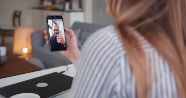 Молода кавказька жінка, яка розмовляє з веселим другом чоловічої статі на самоізоляції за допомогою смартфону онлайн дзвінка. — стокове відео