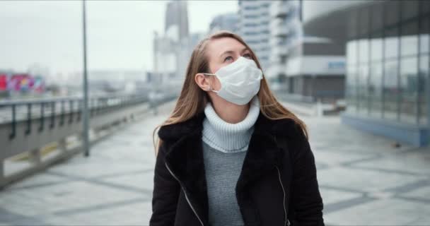 Epidemiskt skydd enligt COVID-19. Ung blond kvinna i medicinsk ansiktsmask går längs tom stadsgata under lockdown. — Stockvideo