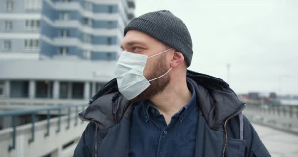 Epidemic protection. Portrait of young bearded Caucasian man wearing medical mask outdoors during coronavirus quarantine — Stock Video