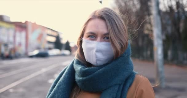 Seuchenbekämpfung. Porträt einer jungen blonden Kaukasierin mit Schutzmaske im Freien auf der Quarantäne COVID-19. — Stockvideo