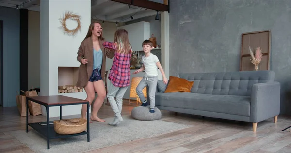 Beautiful happy young Caucasian single mom and two teen age children dancing together, have fun going crazy at home.