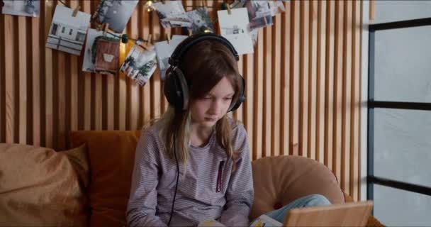 Электронное обучение самоизоляции. Молодая милая белая девочка-подросток самостоятельно учится дома с помощью наушников и ноутбука . — стоковое видео