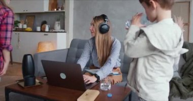 Güzel, beyaz bir anne dizüstü bilgisayarla evde çalışmaya çalışıyor. İlgiye ihtiyacı olan iki genç çocuk dikkatini dağıtıyor.