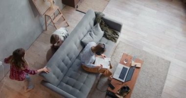 Aile karantinada. Üst düzey anne laptopla evde çalışmaya çalışıyor. İki çocuk yastıklarla boğuşuyor.