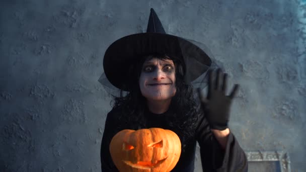 Halloween witch holding a pumpkin and waving his hand — Stock Video