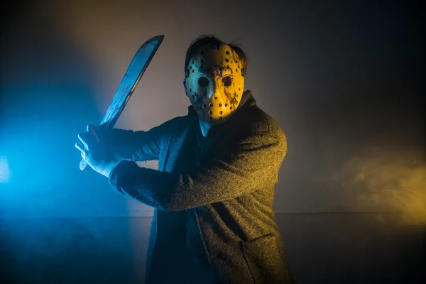 Un tueur en série homme caucasien avec portrait masque en studio de silhouette, masque blanc de hockey effrayant sur jeune homme brandissant une machette — Photo