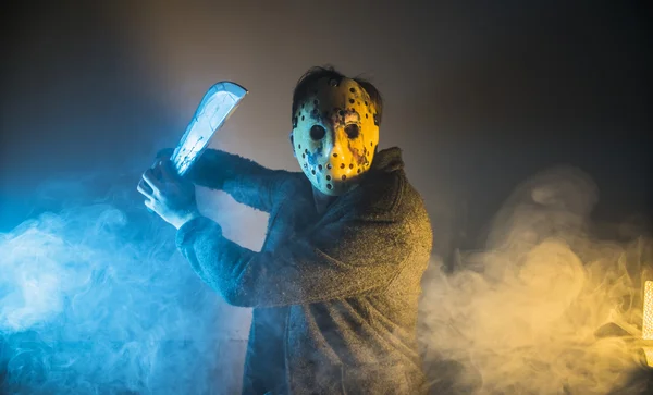 Ein kaukasischer Mann Serienmörder mit Maskenporträt im Scherenschnitt-Studio, gruselige Hockey-Maske auf jungen Mann, der eine Machete droht — Stockfoto