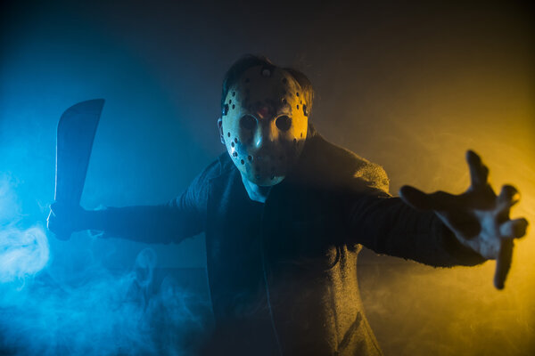 one caucasian man serial killer with mask portrait in silhouette studio, Scary hockey white mask on young man threateningly brandishing a machete