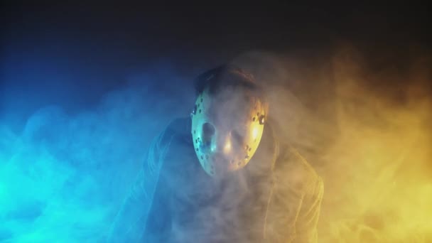 En kaukasisk mannen seriemördare med mask porträtt i silhouette studio, skrämmande hockeymask vit på ung man threateningly svängde en machete — Stockvideo
