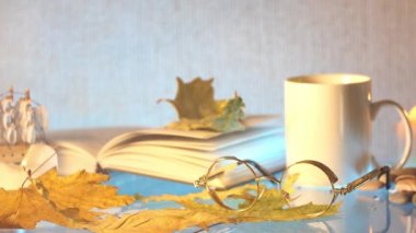 Beyaz çay bardağı, Gözlük, kitap ve gri arka plan üzerinde sonbahar yaprakları