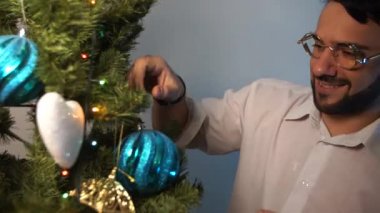 Genç adam giyen santa claus şapka gülümseyen ve Noel ağacı iç dekorasyon