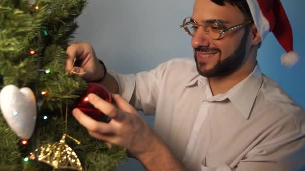 Glimlachend Jongeman Dragen Kerstman Hoed Versieren Kerstboom Binnenshuis — Stockvideo