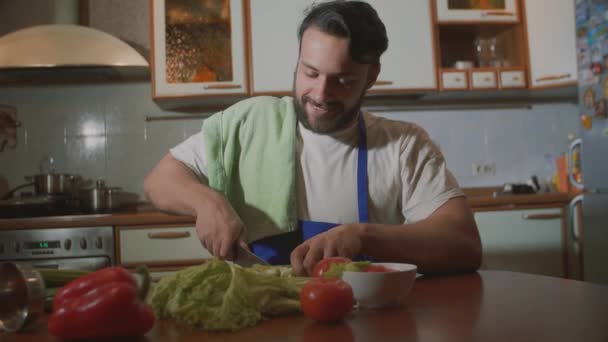 Человек готовит на кухне он режет овощи — стоковое видео