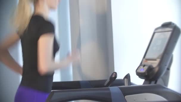 Krásná mladá dívka se zabývá sportovní a fitness, běží na běžeckém pásu simulátor — Stock video