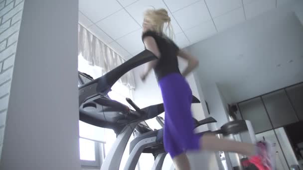 Beautiful young girl is engaged in sports and fitness, she runs on the simulator treadmill — Stock Video