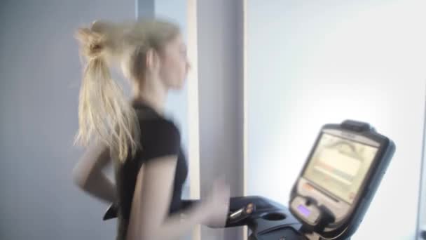 Vacker ung flicka är engagerade i sport och fitness, hon springer på löpbandet simulator — Stockvideo