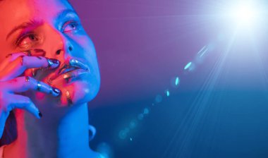 Model metalik gümüş dudaklar ve neon mavisi ve mor renkli yüzlü kadın, stüdyoda poz veriyor, güzel kız, parıldayan makyaj, renkli.