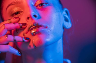Model metalik gümüş dudaklar ve neon mavisi ve mor renkli yüzlü kadın, stüdyoda poz veriyor, güzel kız, parıldayan makyaj, renkli.