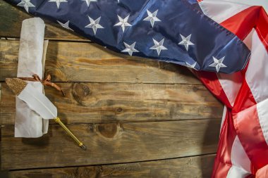 USA flag and ancient manuscript. Rolled-up constitution document on national flag of America, wooden background. Declaration of the Independence of the United States and national flag