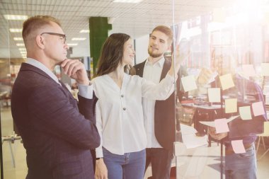 Dört iş adamı tartışıyor ve plan yapıyor. Cam duvar işareti ve çıkartmaların önünde. Başlangıç ofisi